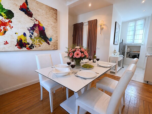 A dining area with a white table set for four, a vase of flowers, and a painting on the wall.