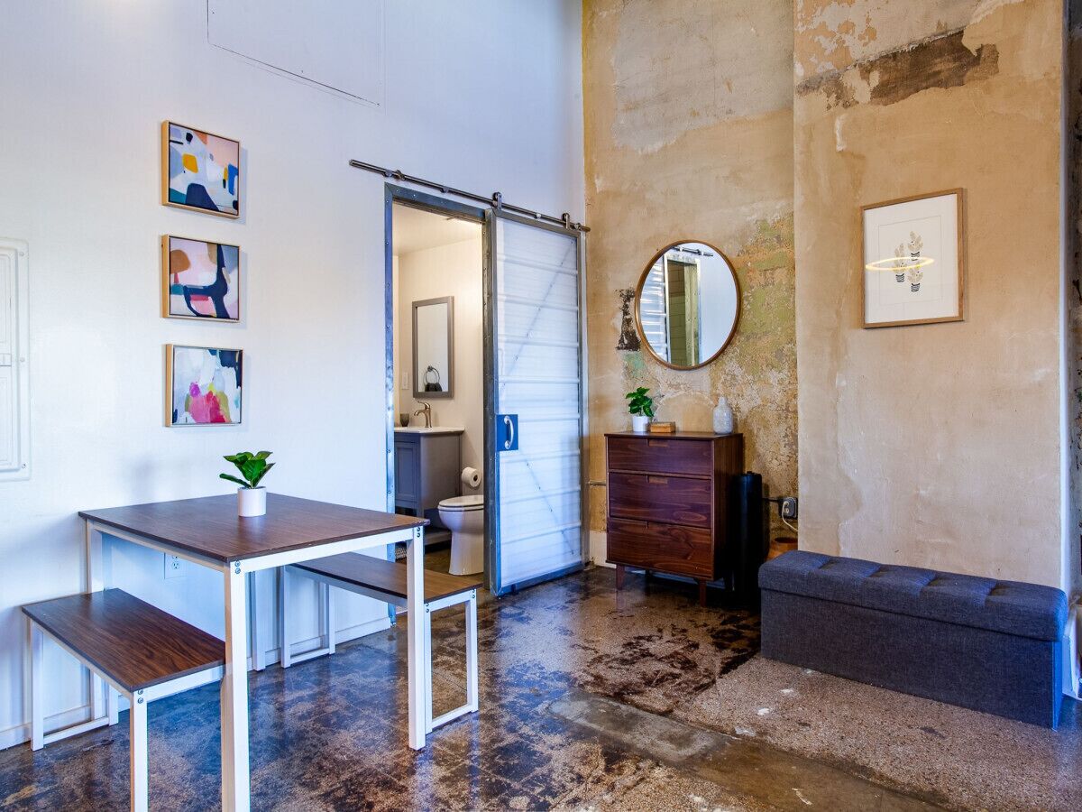 Une pièce avec une table en bois, un banc, une commode et un miroir au mur.