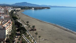 Un paysage urbain côtier avec une vaste plage, un ciel bleu dégagé et une montagne en arrière-plan.