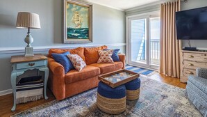 A living room with a sofa, a side table, a lamp, a framed painting, a television, and a window with curtains. - Recently renovated condo in Cherry Grove area of N. Myrtle Beach (North Myrtle Beach)