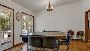 A dining area with a long wooden table, four black chairs, a chandelier, and a clock on the wall.
