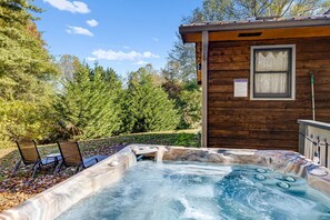 A wooden cabin with a hot tub, two lounge chairs, and a sign indicating no tub usage.