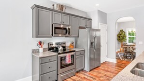A modern kitchen with grey cabinets, stainless steel appliances, and a wooden floor.
