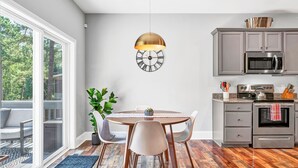 A modern kitchen with a round dining table, white chairs, and a large clock on the wall.