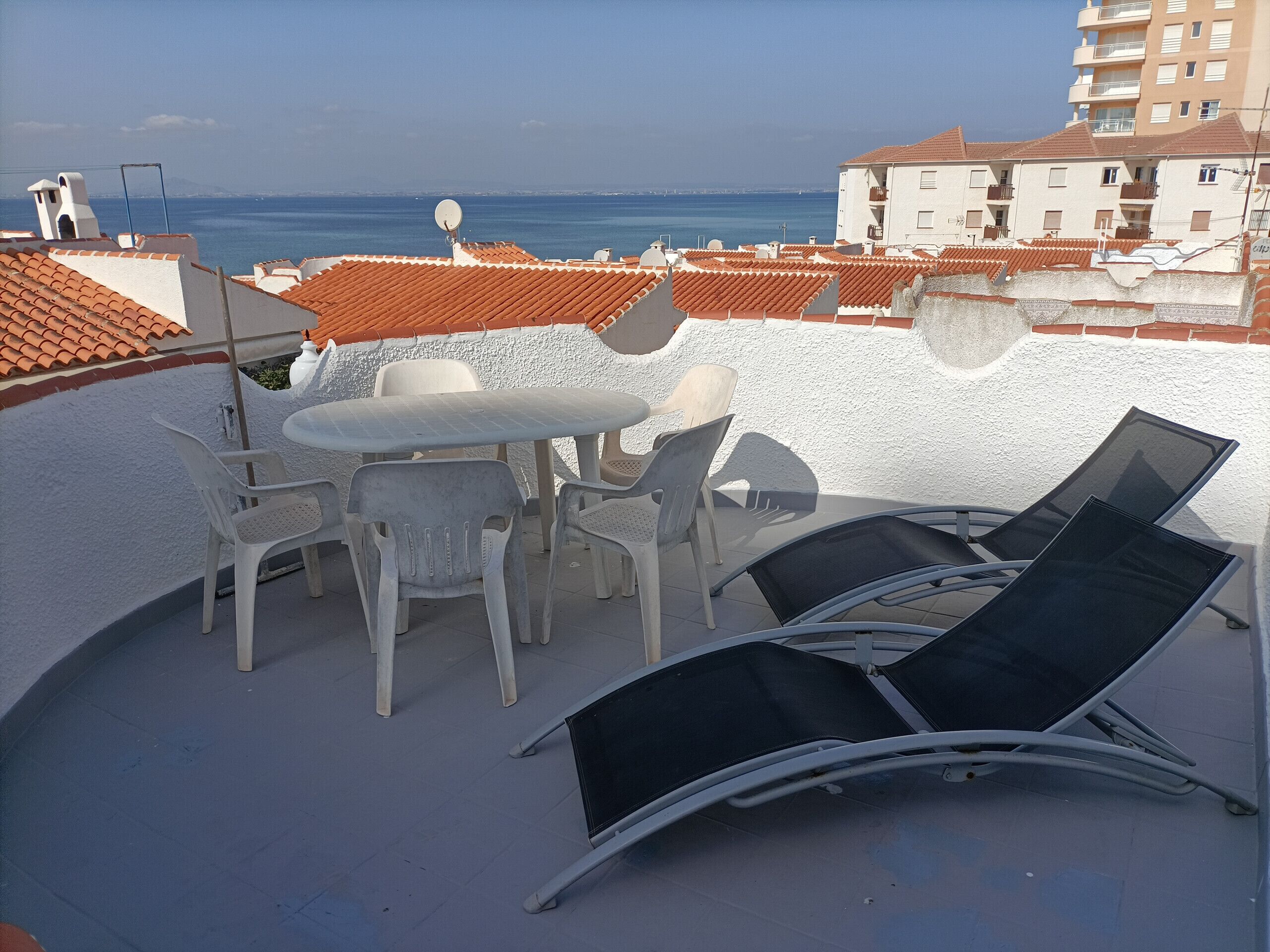 A rooftop terrace with a table and chairs, overlooking a coastal cityscape.