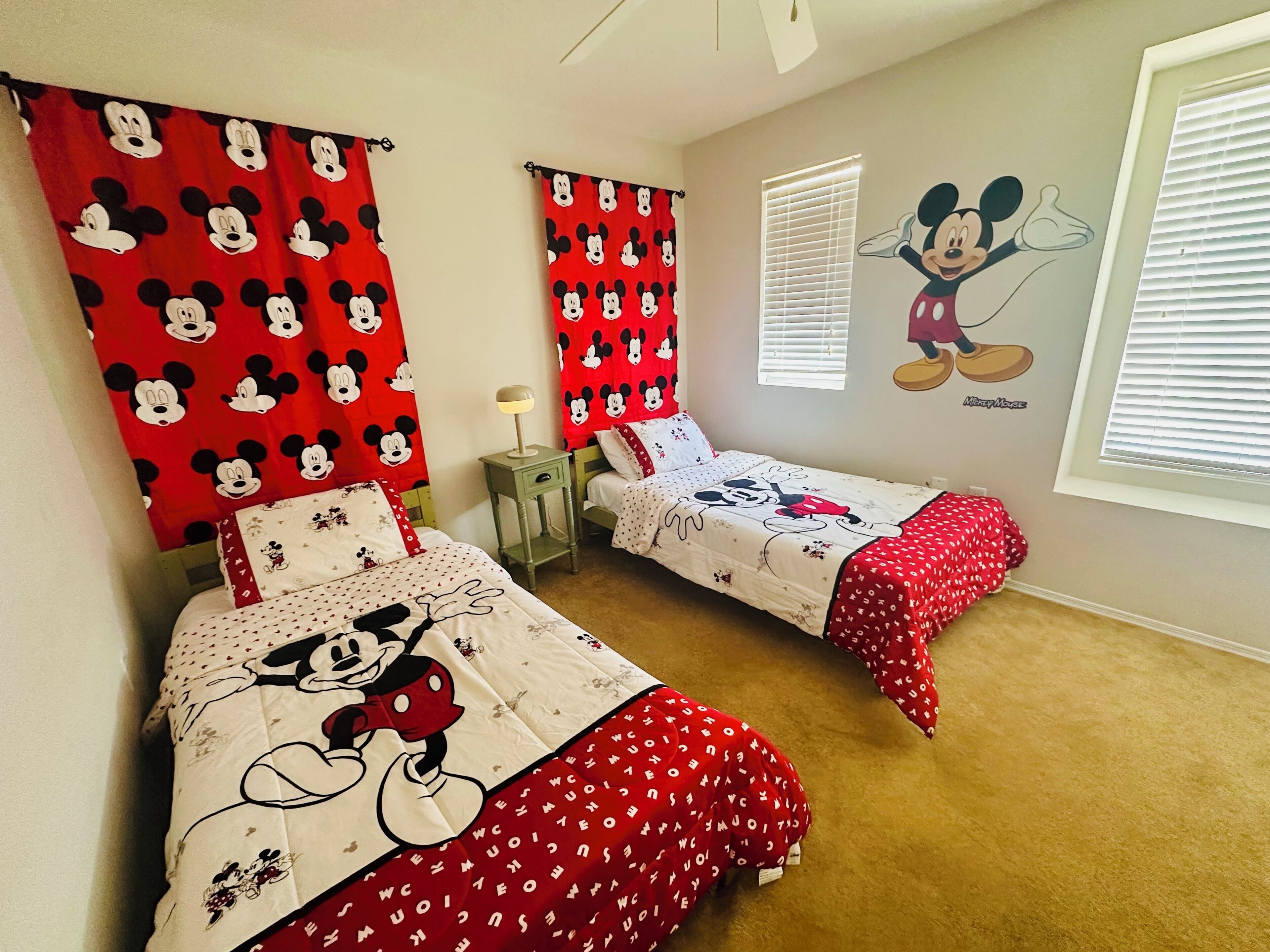 Un dormitorio con dos camas, cada una con ropa de cama y cortinas con temática de Mickey Mouse, además de un mural en la pared de Mickey Mouse.