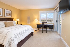 A bedroom with a bed, desk, and window with a view.