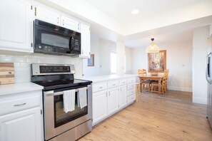 A modern kitchen with white cabinets, a stainless steel oven, and a microwave. There is a dining area with a wooden table and chairs. - Waterpark resort with basketball, pickleball court (St. George)