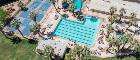 An aerial view of a resort with a large swimming pool, tennis courts, and palm trees.