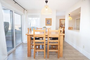 A dining area with a wooden table and chairs, a large window with a view, and two pendant lights.