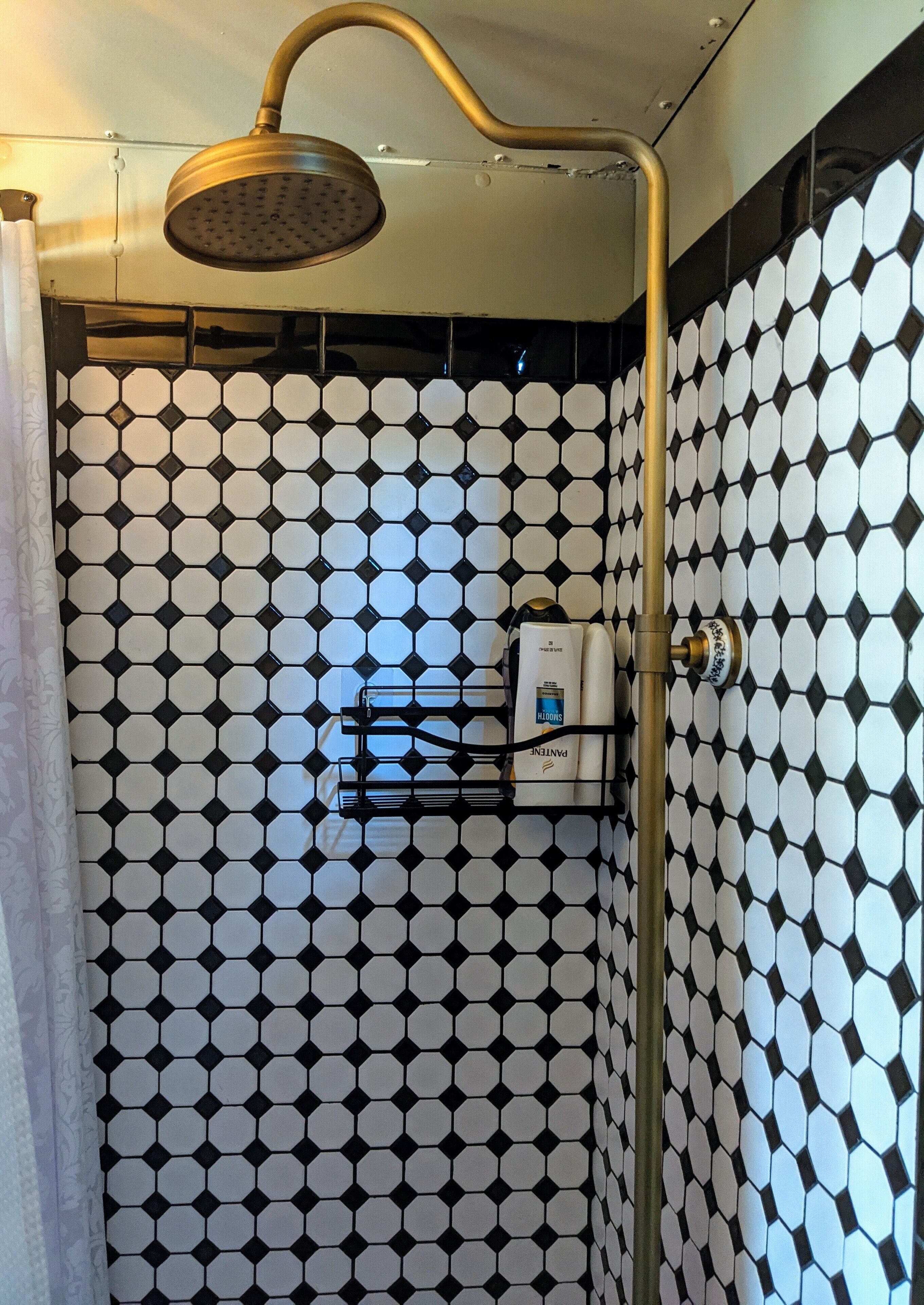 A shower with a gold shower head and a black and white hexagonal tile wall.