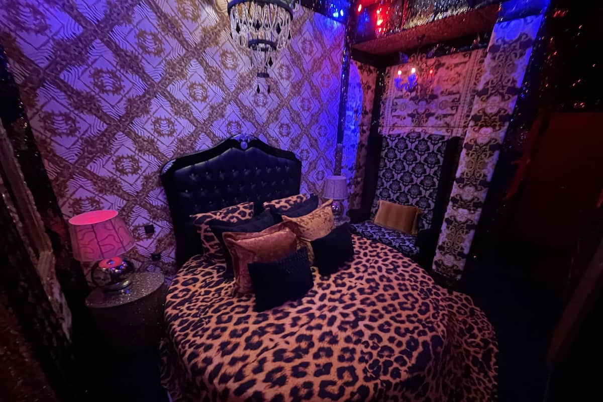 A room with a bed featuring a leopard print bedspread, a tufted headboard, and multiple pillows.