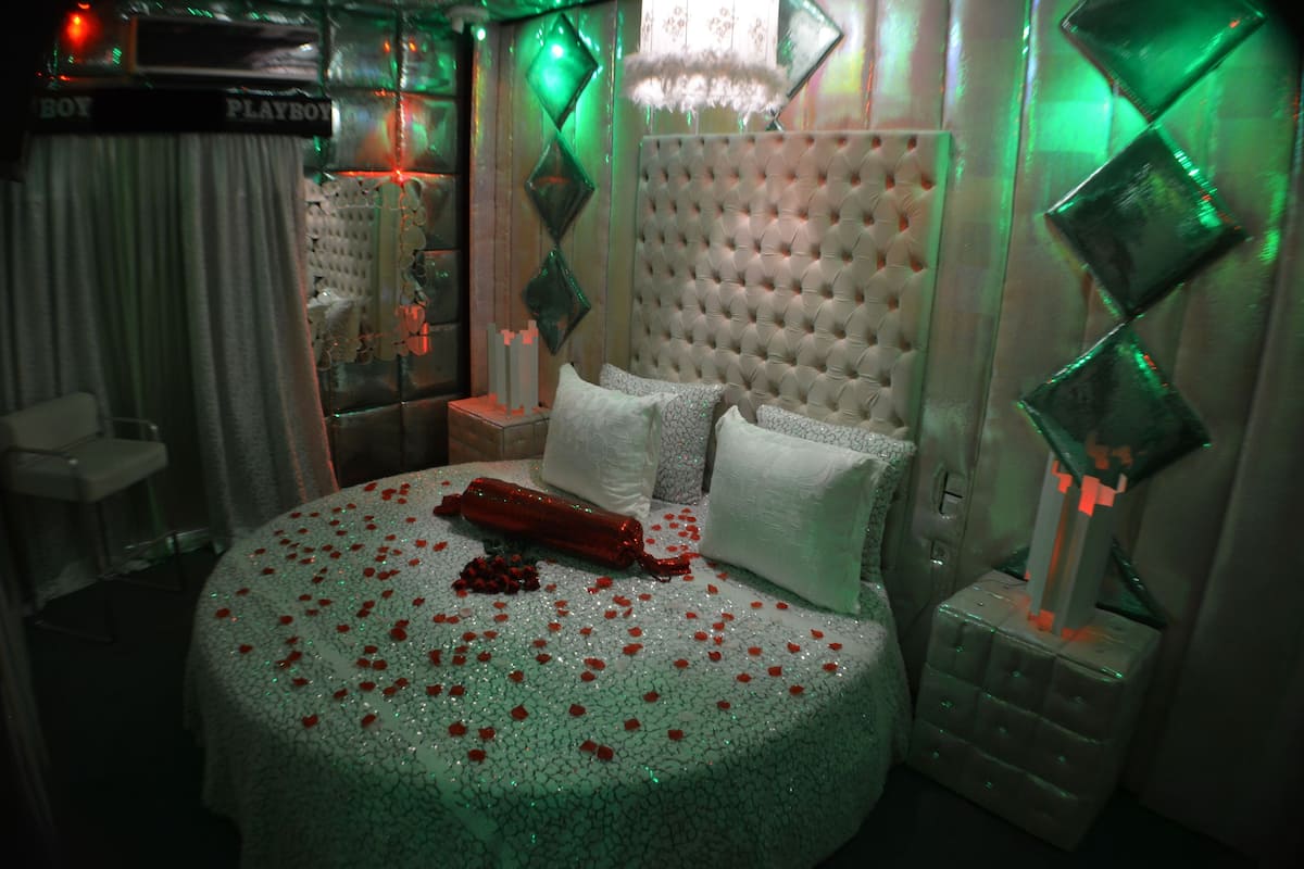A bedroom with a tufted headboard, a bed with rose petals, and diamond-shaped wall decorations.