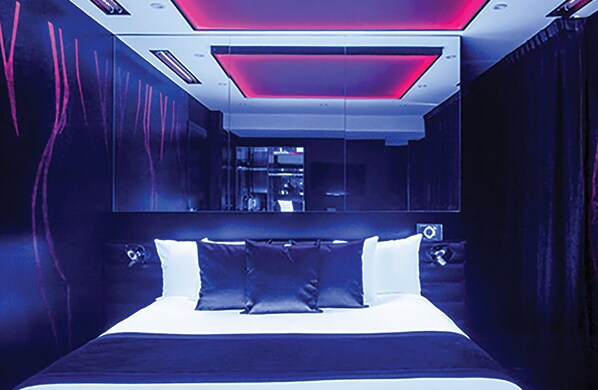 Quarto moderno com uma cama grande, um espelho sobre a cama e uma luz vermelha decorativa.