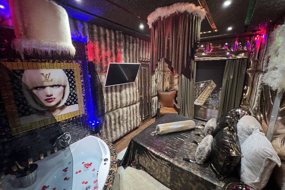 A luxurious bathroom with a large mirror, a bathtub with rose petals, a plush chair, and decorative elements like a feathered headpiece and a Louis Vuitton pattern.