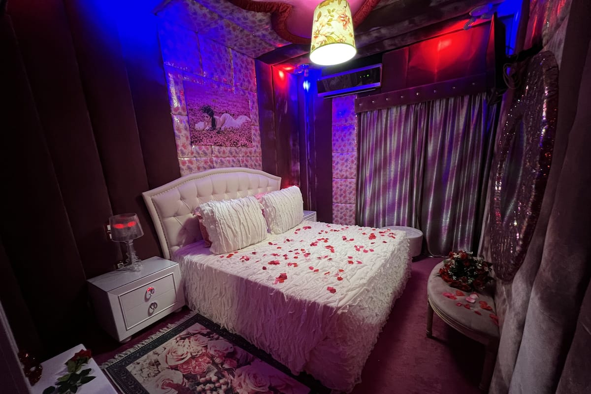 A bedroom with a large bed, a nightstand, a lamp, and a floral rug.