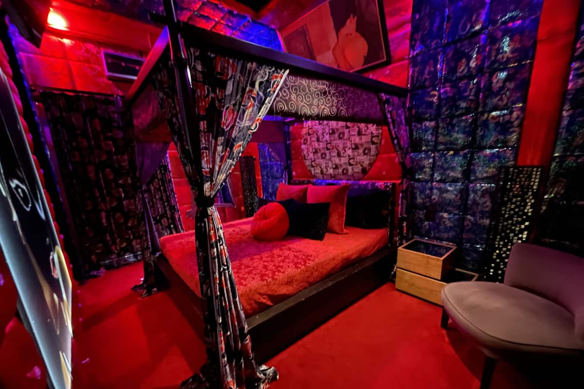 A room with a canopy bed, red bedding, and patterned wall art.