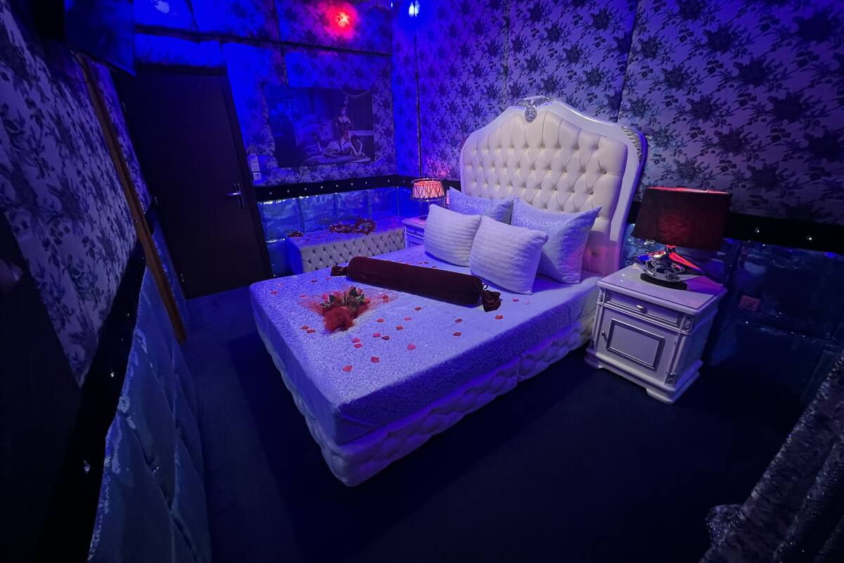 A bedroom with a tufted headboard, white bedding, and a bedside table with a lamp.