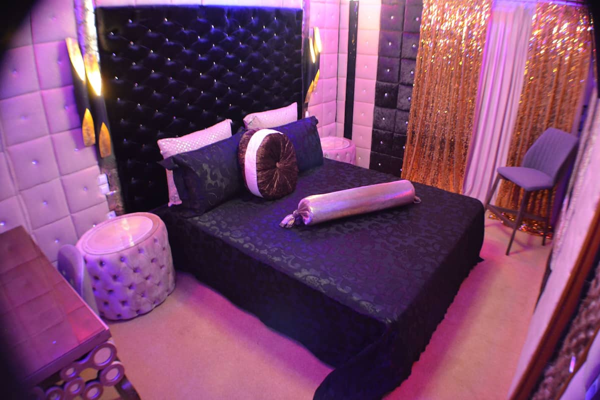 A bedroom with a tufted headboard, a bed with patterned bedding, a side table, and a chair.