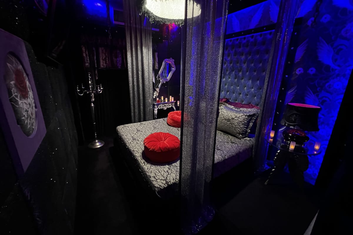 A dimly lit room with a bed, a mirror, and a chandelier.
