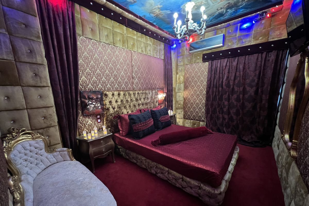A luxurious bedroom with a large bed, ornate headboard, and a chandelier.