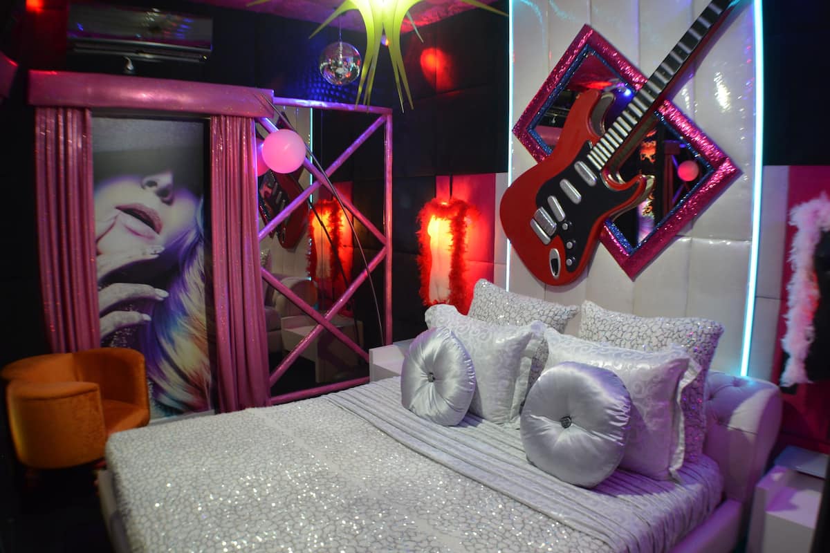 A bedroom with a bed, pillows, a guitar, and a mirror.