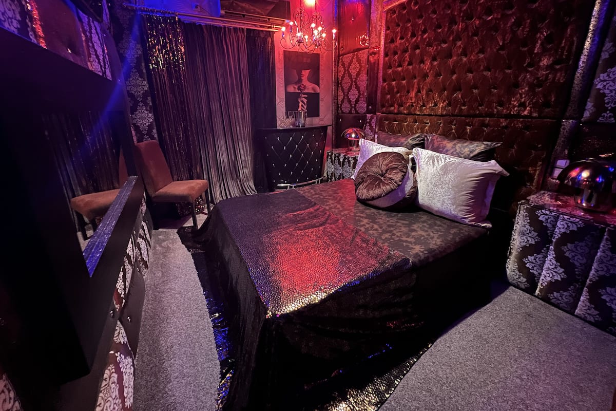 A dimly lit room with a bed, a chair, and a table with a lamp.