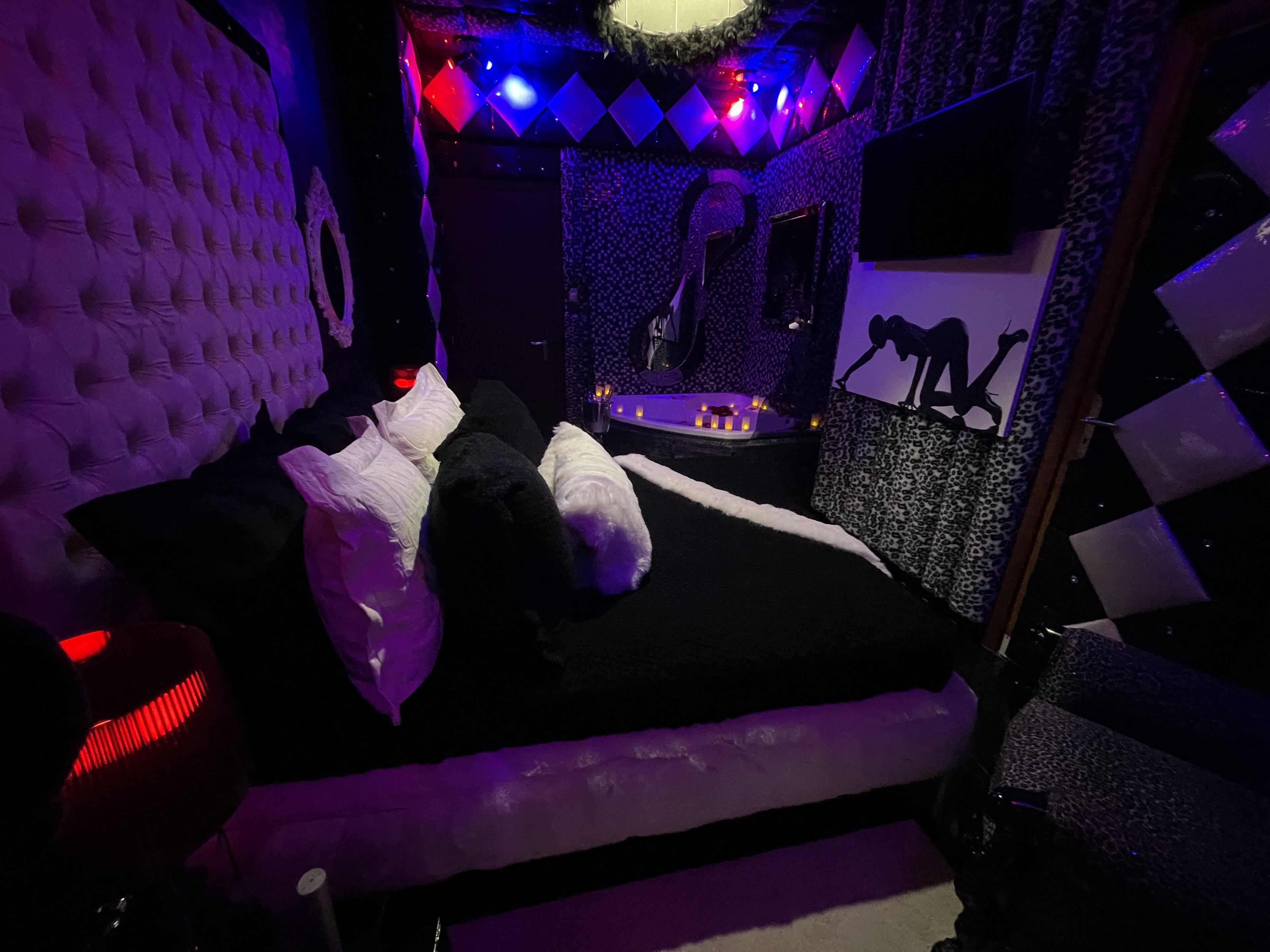 A room with a tufted headboard, a bed with white and black bedding, a small table with candles, and a leopard print wall.