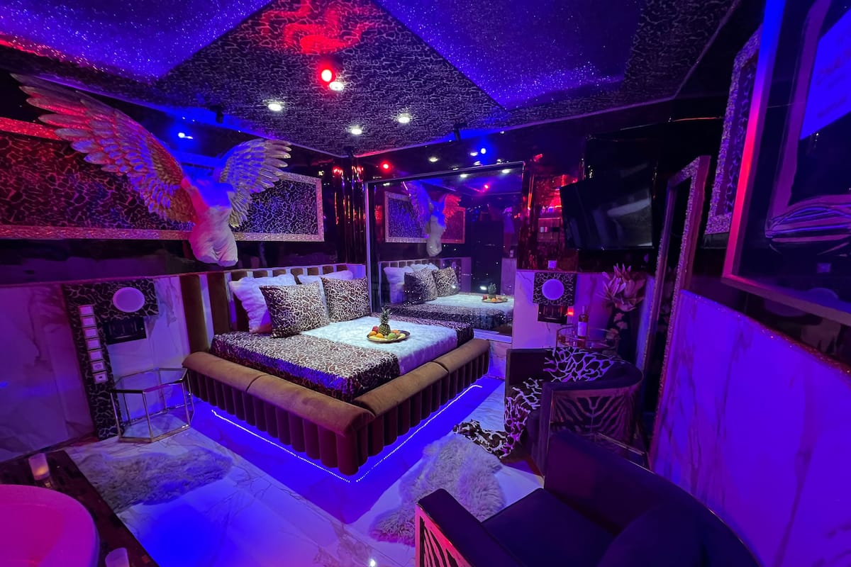 A room with a central bed, a small seating area, and a large mirror.