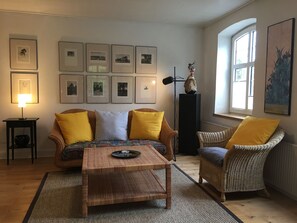 Una sala de estar con un sofá, dos sillones, una mesa de centro y cuadros en la pared.