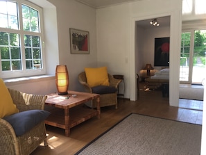 Amplia sala de estar con muebles de mimbre, una mesa de centro de madera y un gran ventanal que proporciona luz natural.