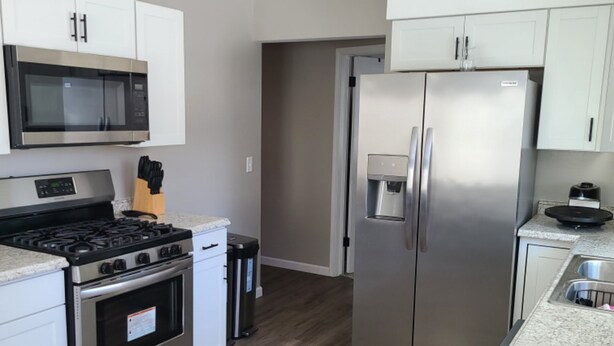 Una cucina moderna con elettrodomestici in acciaio inossidabile, mobili bianchi e pavimento in legno.
