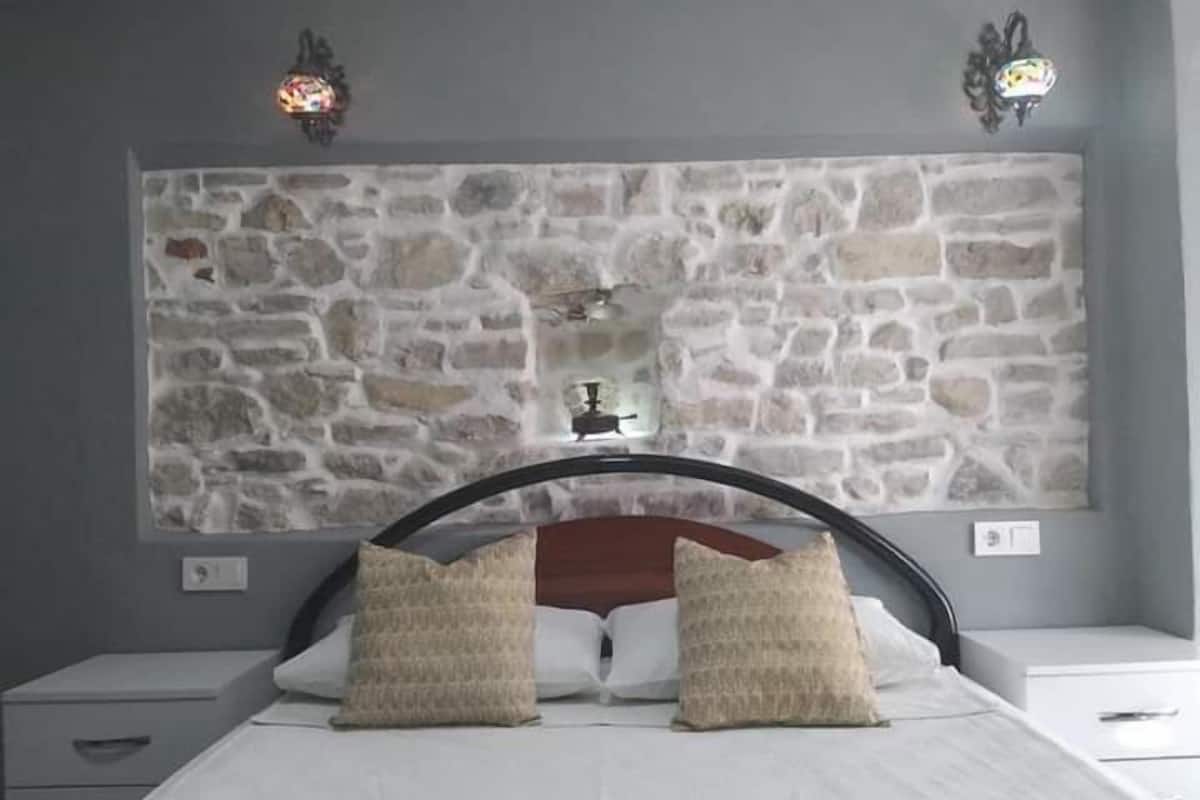 Une chambre avec une tête de lit en pierre, deux tables de chevet et deux oreillers.