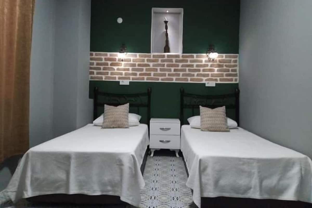 Une chambre avec deux lits, un mur en briques apparentes et un miroir au-dessus des lits.