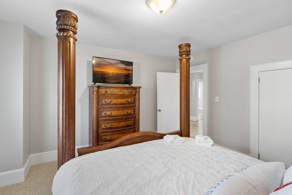 A bedroom with a bed, wooden dresser, and a painting on the wall.