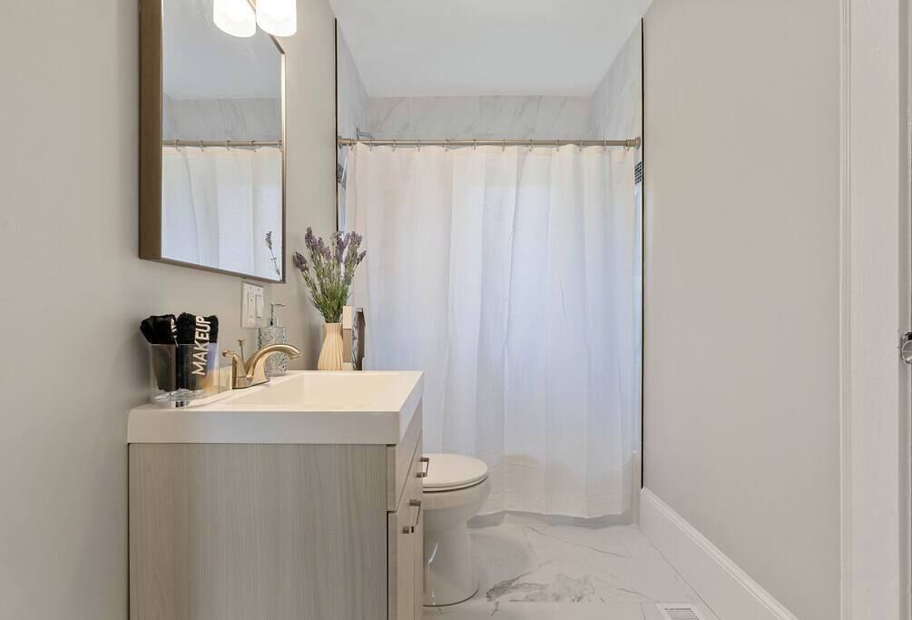 Een moderne badkamer met een witte wastafel, een grote spiegel en een douchegordijn.