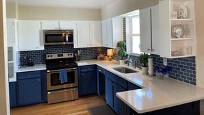 A modern kitchen with white and navy blue cabinets, stainless steel appliances, and a backsplash of dark tiles. - Beachside Daytona Beach Shores 5 min walk to beach, restaurants and more! (Port Orange)