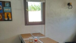 A small, dark-colored table with a glass top and four stools, positioned under a window with a blind. - Comfortable air-conditioned studio in a quiet villa 15 km from Cannes (Peymeinade)