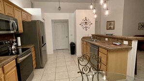 A kitchen with a refrigerator, stove, microwave, and wooden cabinets. There is a dining table with chairs and a chandelier above. - 🏝Beaches, Nature Sanctuaries, and Rockets with plenty of room for a family. (Palm Bay)
