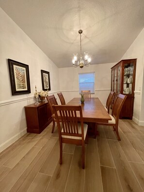 A dining room with a wooden table, chairs, a chandelier, framed artwork, and a cabinet with glass doors. - 🏝Beaches, Nature Sanctuaries, and Rockets with plenty of room for a family. (Palm Bay)
