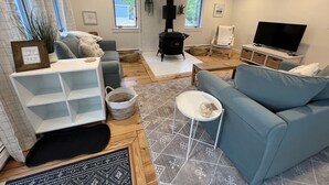 A modern living room with a fireplace, a television, and a comfortable seating area. - Coastal Cape Hideaway - Outdoor Shower & Fire-pit! (Mashpee)