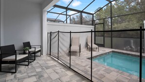 Un área de piscina interior con cerramiento de vidrio, asientos y una pequeña mesa con una planta.