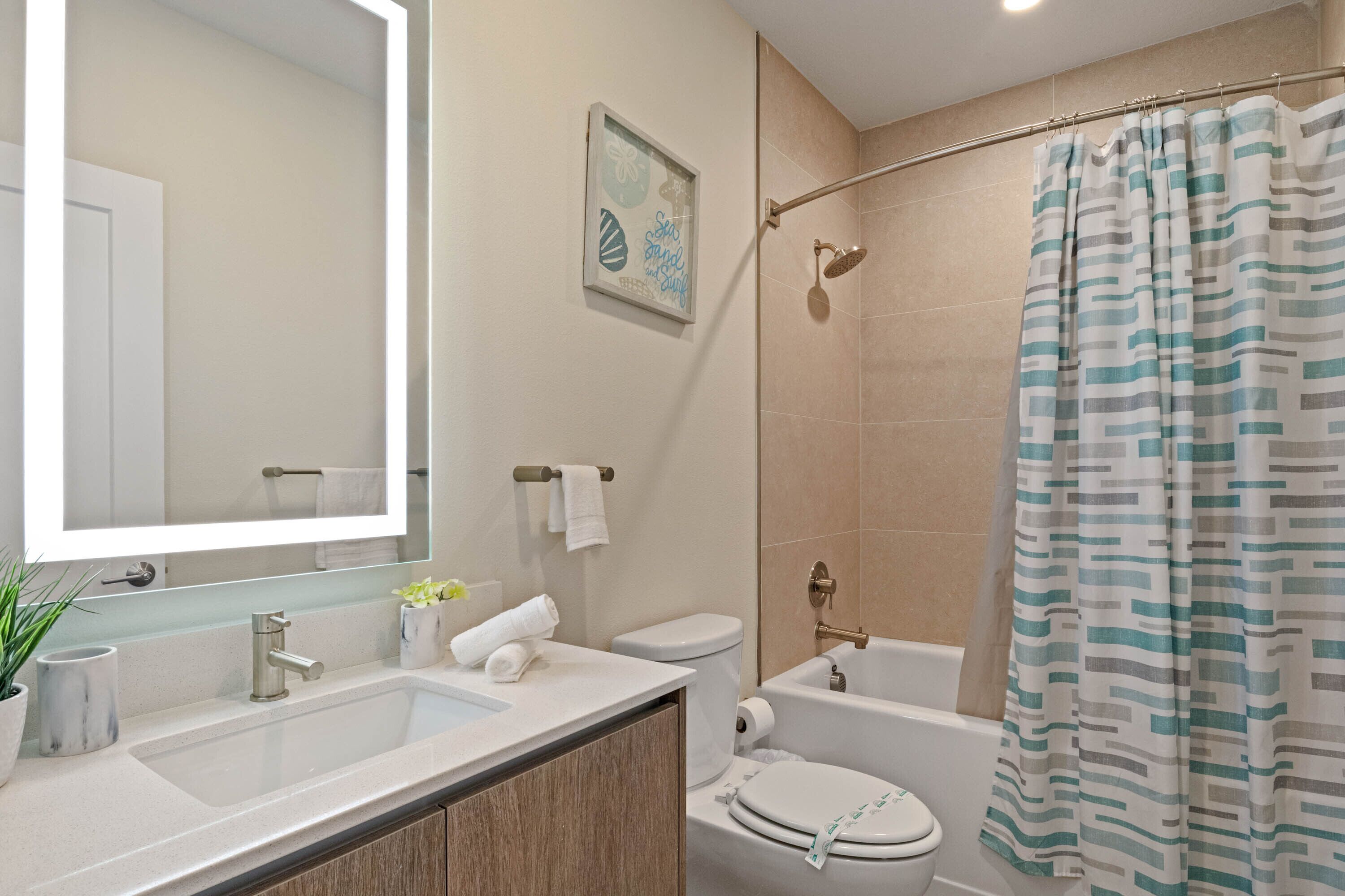 A modern bathroom with a double sink, toilet, bathtub, and shower curtain.