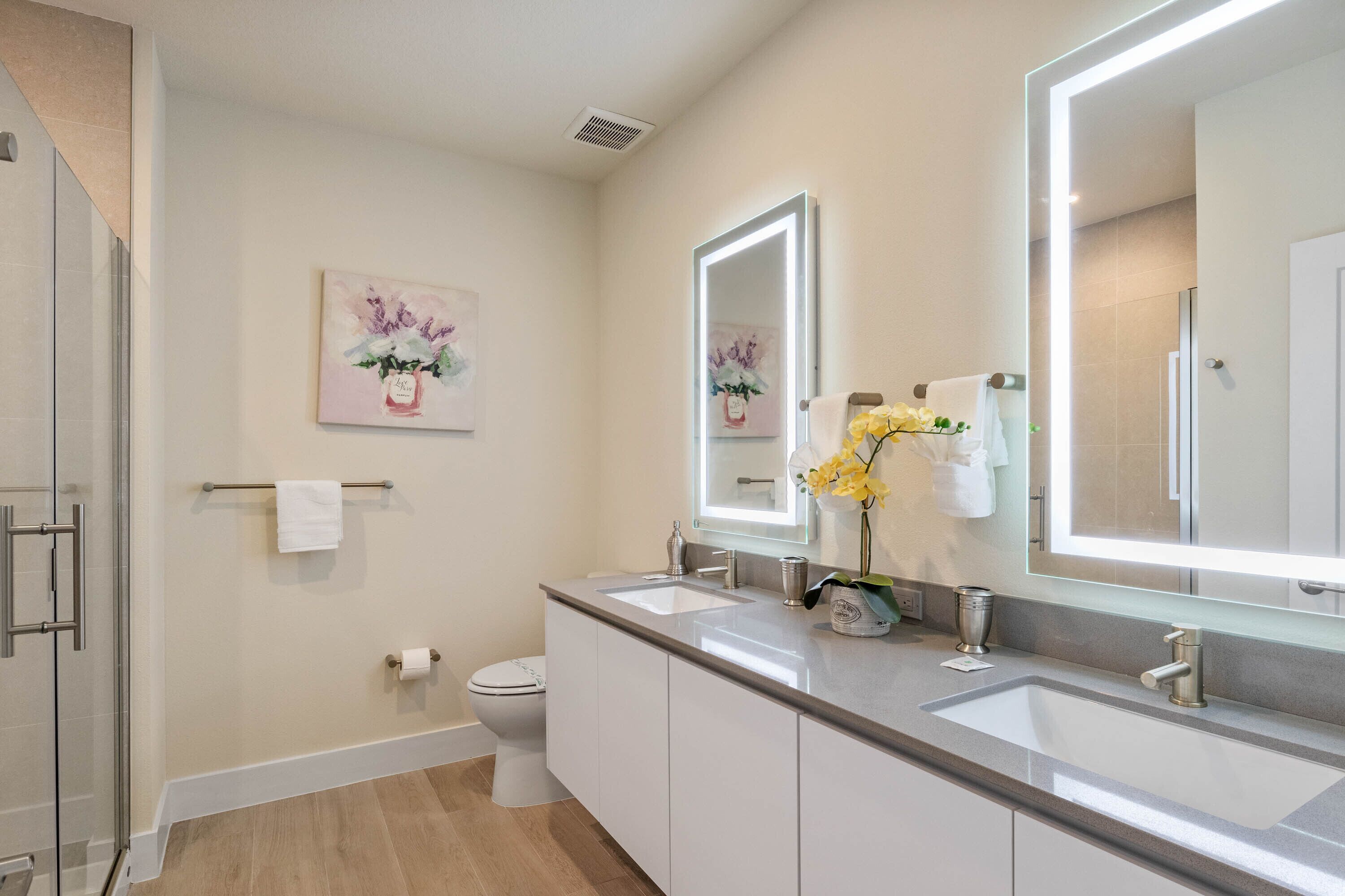Un bagno moderno con uno specchio grande, due lavandini, un water e una doccia.