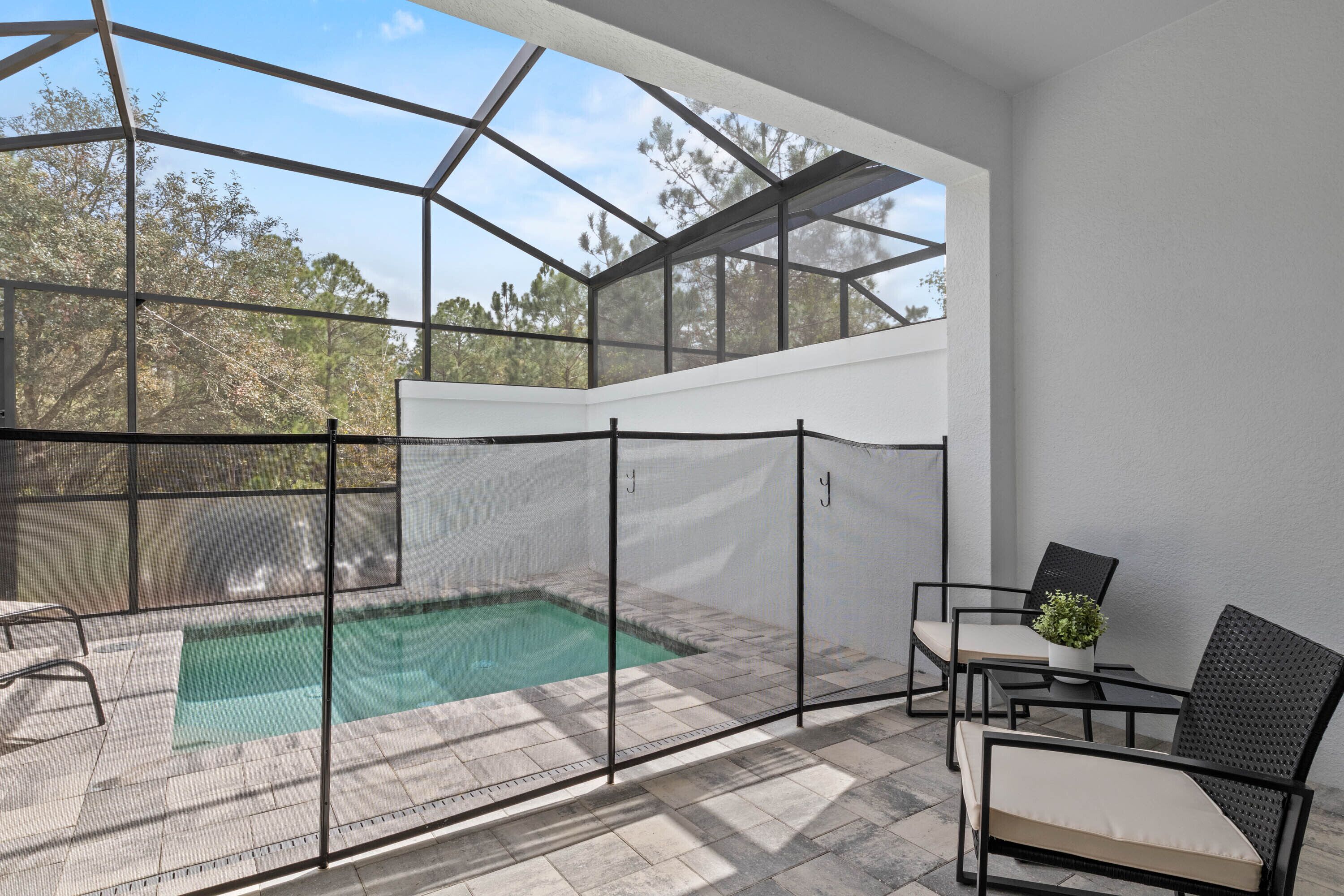A covered outdoor pool area with a glass enclosure, seating, and a small table with a plant.