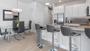 A modern kitchen with white cabinets, stainless steel appliances, and a bar area with bar stools. - Jose's Tikki Room near Disney (Clermont)