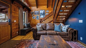 Ein Interieur einer Holzhütte mit einem Ledersofa, einem Holztisch und einer Treppe.