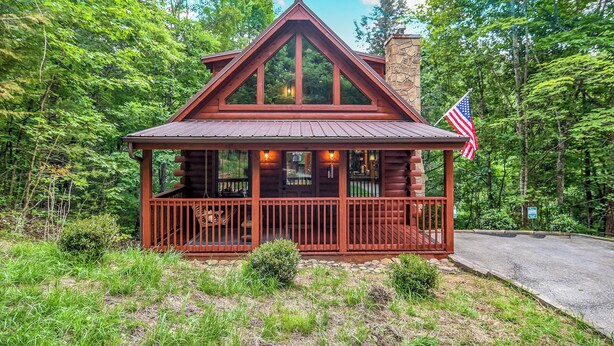 Eine Holzhütte mit einem Steinkamin, einer Veranda mit Geländern und einer amerikanischen Flagge.