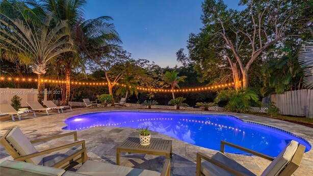 Una piscina con sillones de descanso y luces colgantes.