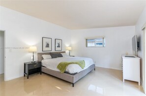 A bedroom with a bed, nightstands, a TV, and a window. - Amazing backyard for Family vacation with heated pool.  (Wilton Manors)